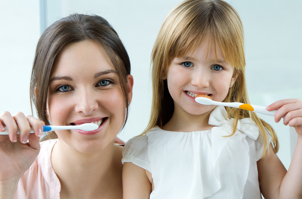 Mother and daughter brushing their teeth together to promote oral hygiene