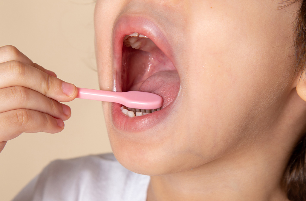 A young boy cleaning his tongue with a toothbrush to remove bacteria and prevent bad breath