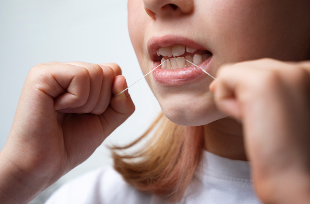 A young girl flossing teeth to remove bacteria and prevent gum disease